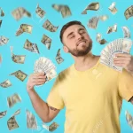 126900406 happy young man with dollars under money rain on blue background